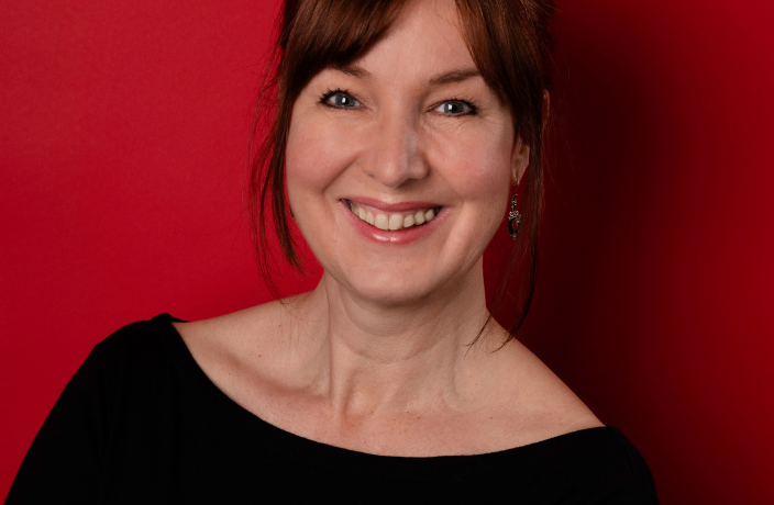 Jo Lochhead smiles at the camera in front of a red background