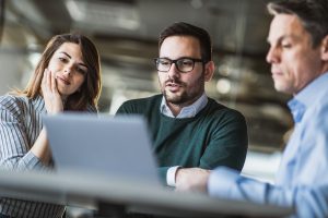 Two men and a woman looking at a laptop